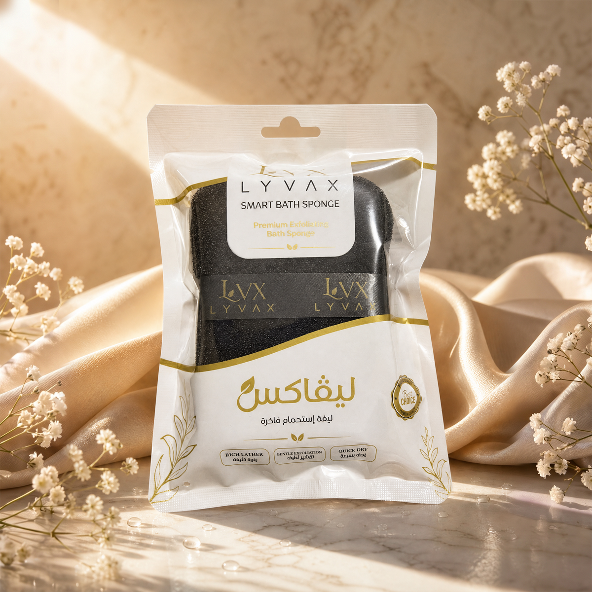A package of LYVAX Smart Bath Sponges in black, presented in a premium white and gold foil bag with Arabic text, styled on a marble surface with draped champagne silk and small white flowers.
