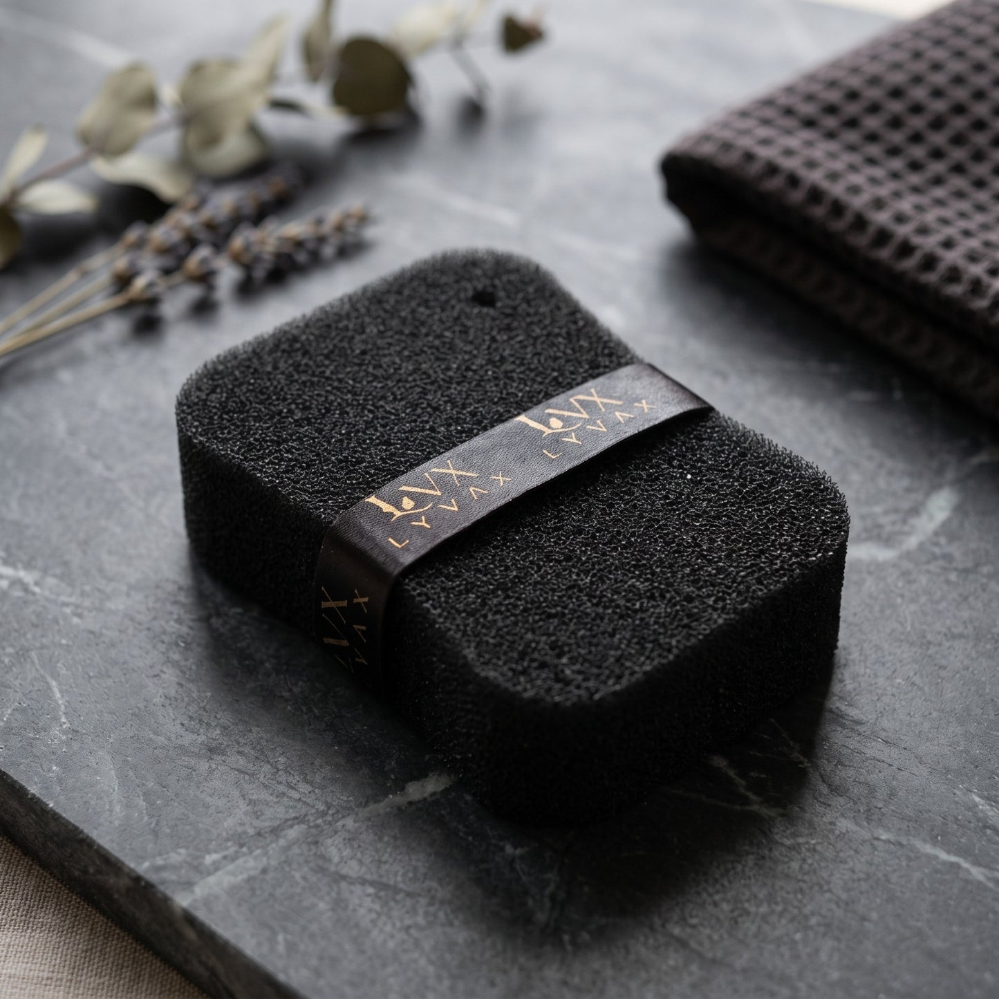 LYVAX Smart Bath Sponge close-up showing porous texture and branded ribbon on dark marble