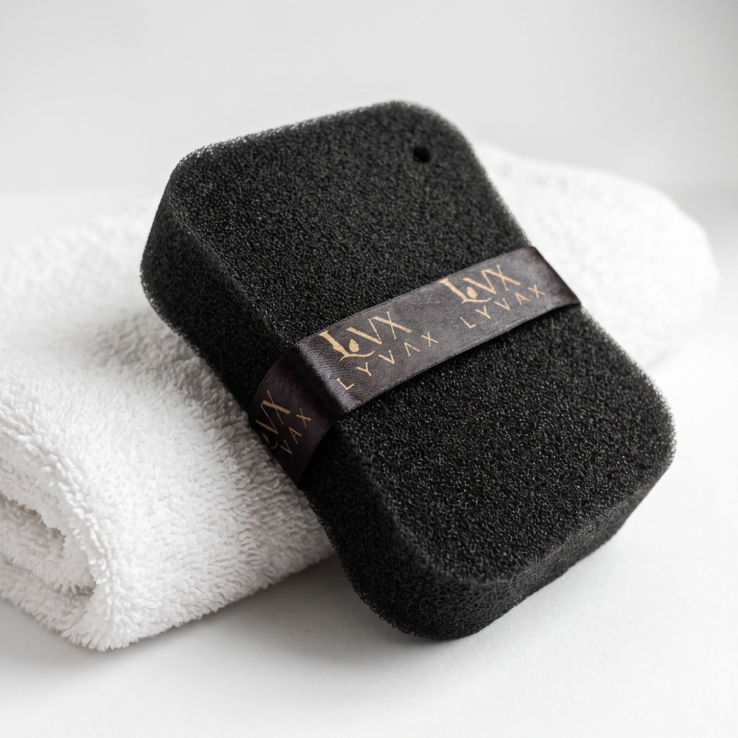 LYVAX Smart Bath Sponge leaning on white towel showing open-cell texture and hanging ribbon