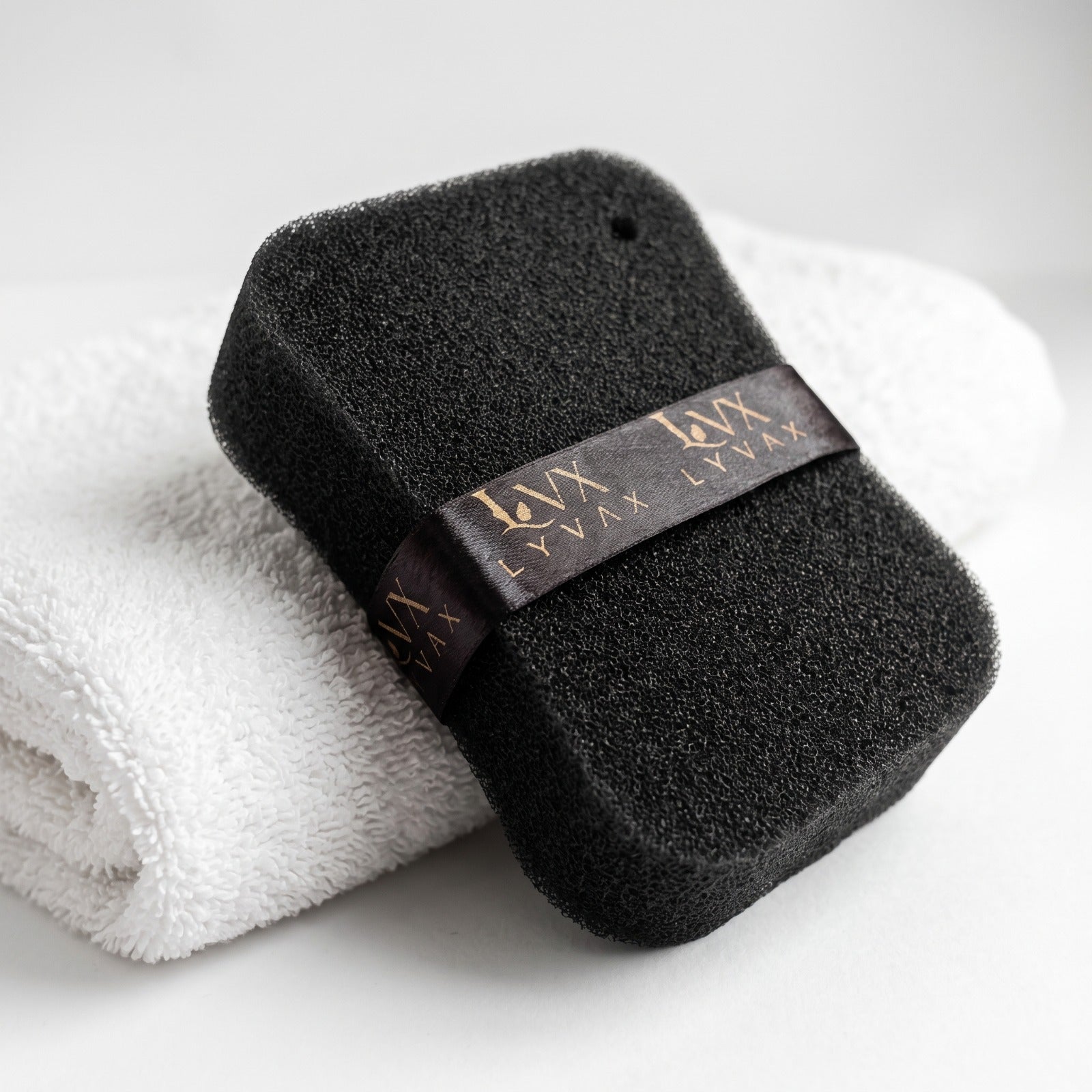 LYVAX Smart Bath Sponge leaning on white towel showing open-cell texture and hanging ribbon