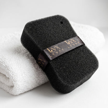 LYVAX Smart Bath Sponge leaning on white towel showing open-cell texture and hanging ribbon